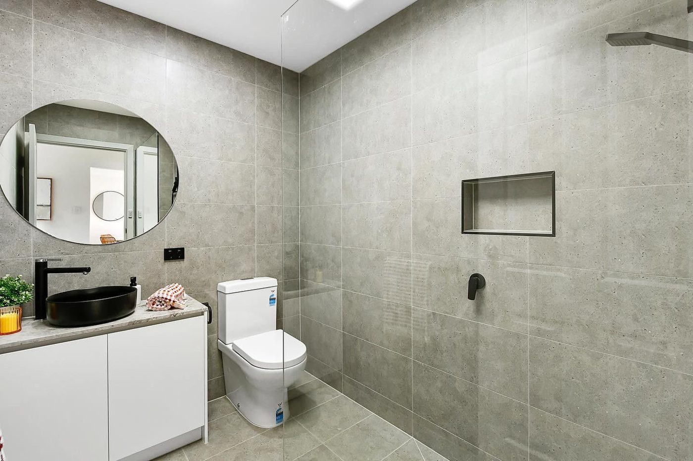 Grey-tiled bathroom with round mirror and black tapware, Keysborough